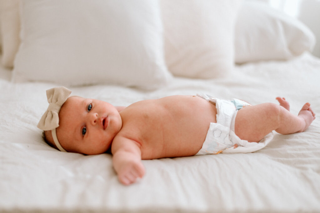 newborn baby in diaper and bow laying on a bed