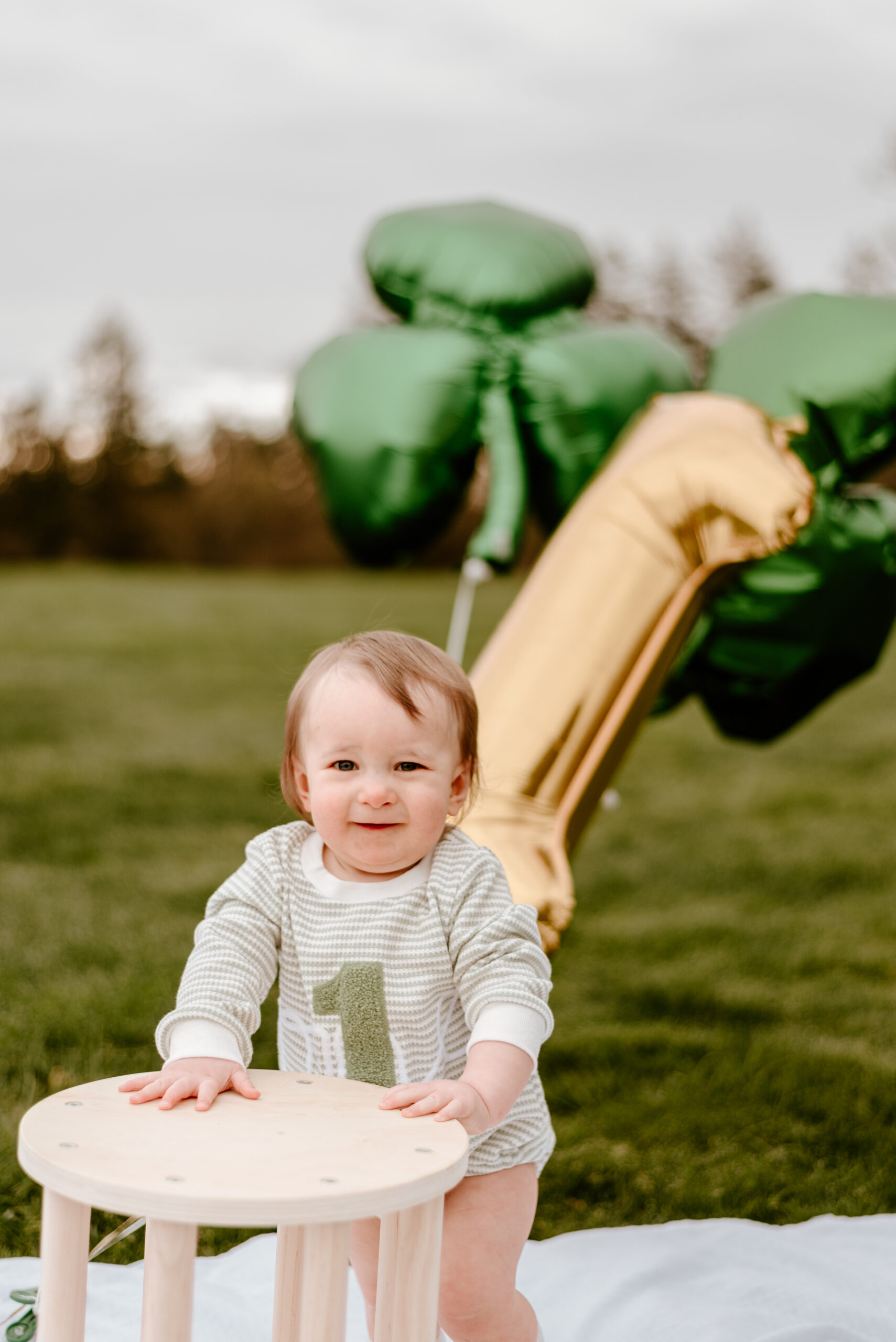 one year old stands up on a blanket with balloons in the background