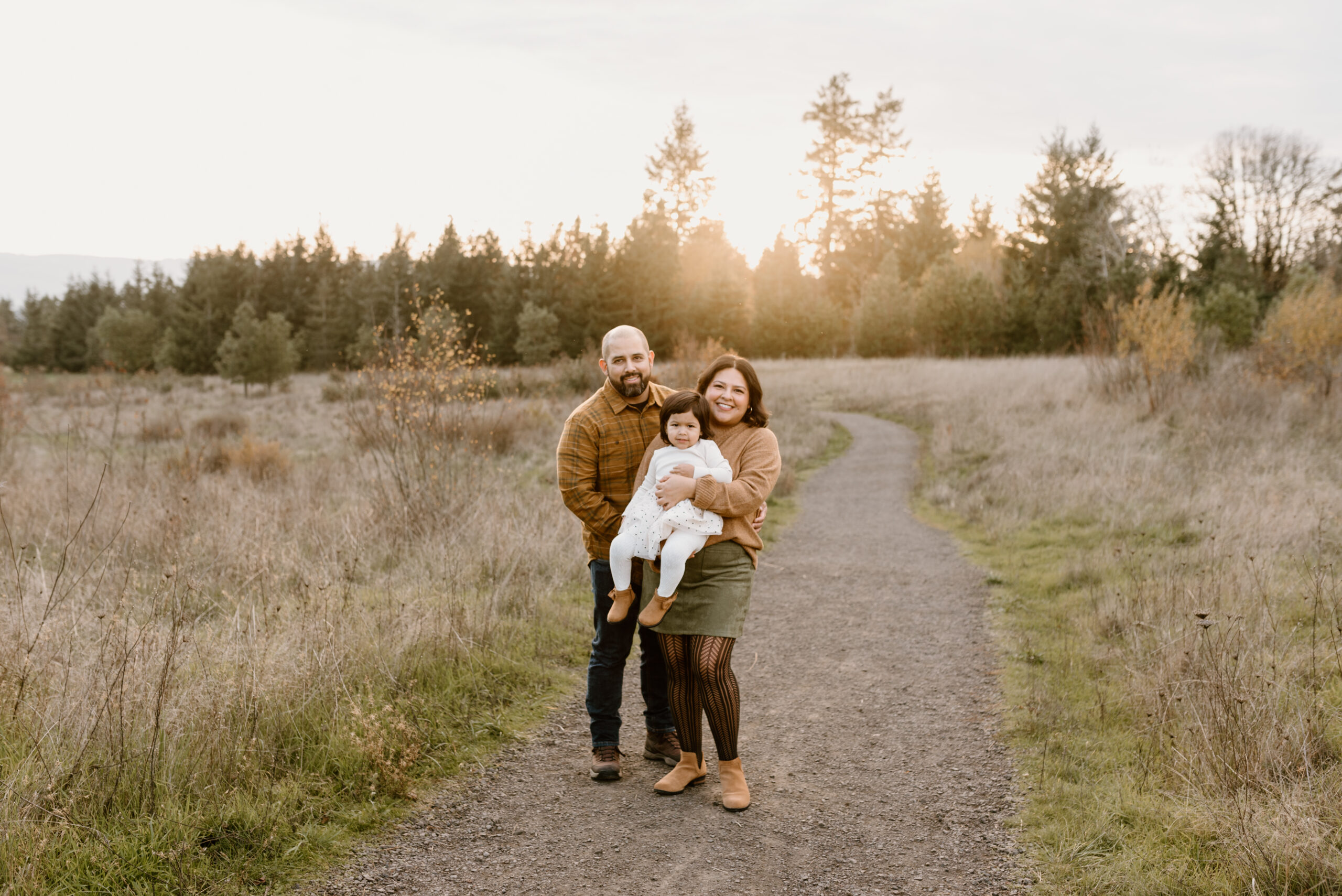 family standing in a path holding a toddler and smiling at the camera