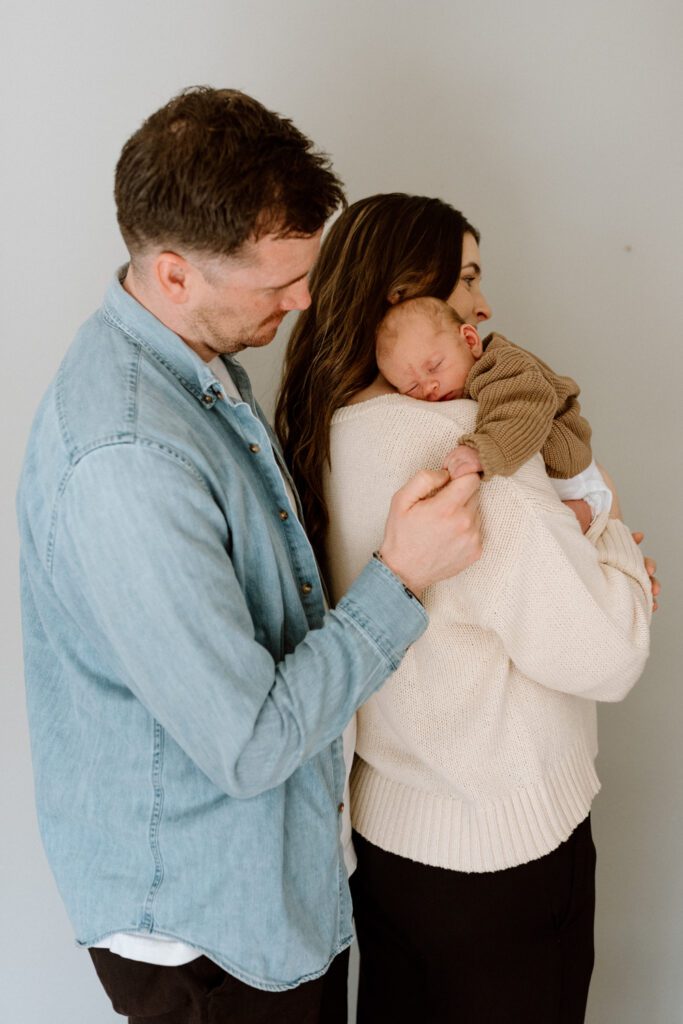 family snuggling a newborn while dad and baby hold hands